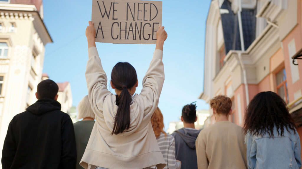 Asian woman in back of protest demonstration holding a poster We need a change. Student activist